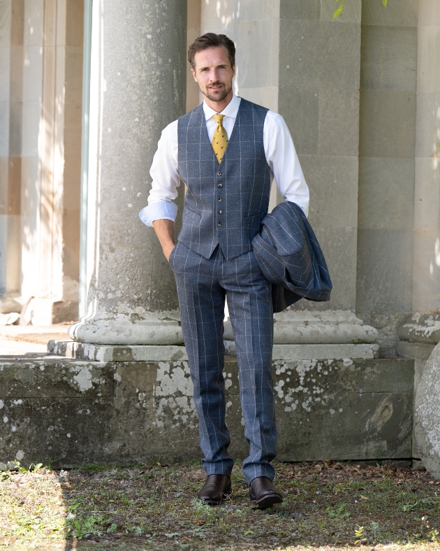 A man standing with his hands in his pockets while holding a striped jacket that matches his trousers and waistcoat